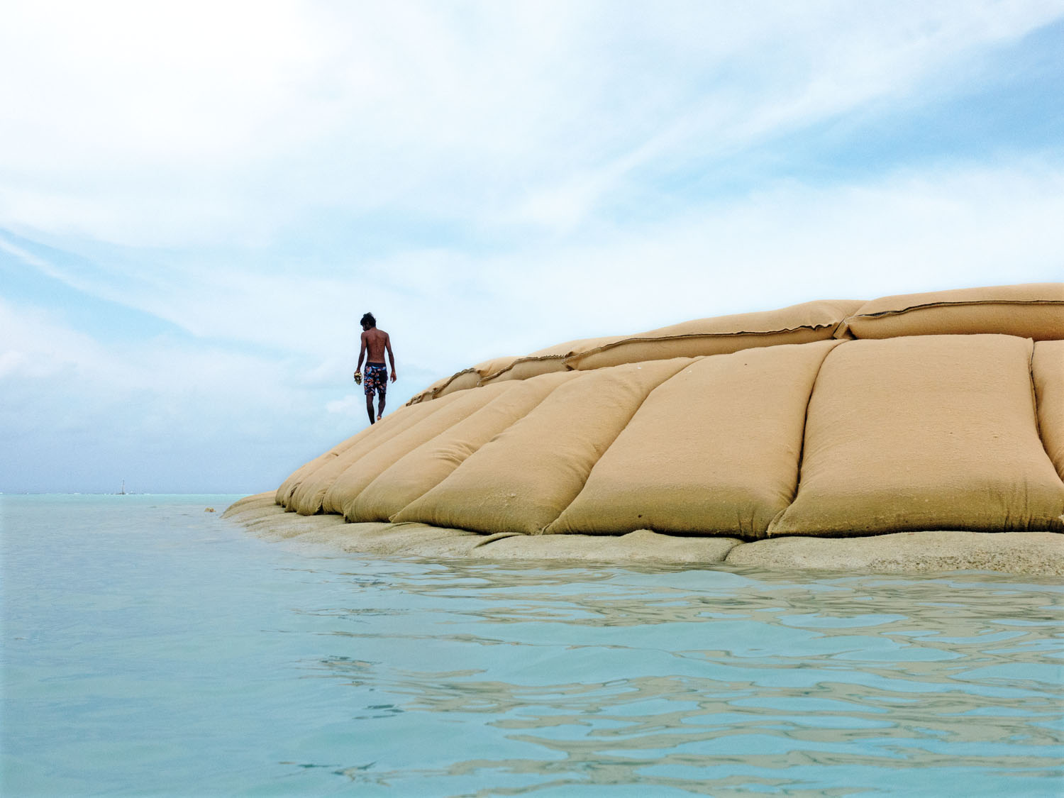 Ahmed Aiham, a local environmental activist, walks over a dike of geotextile bags protecting a land-reclamation project on the island of Fulhadhoo.