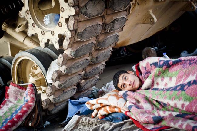 A boy rests under the treads of an Egyptian army tank in Tahrir Square, in downtown Cairo. Protesters gathered there beginning on January 25, 2011, calling for the ouster of President Hosni Mubarak, who had ruled the country unopposed since 1981
